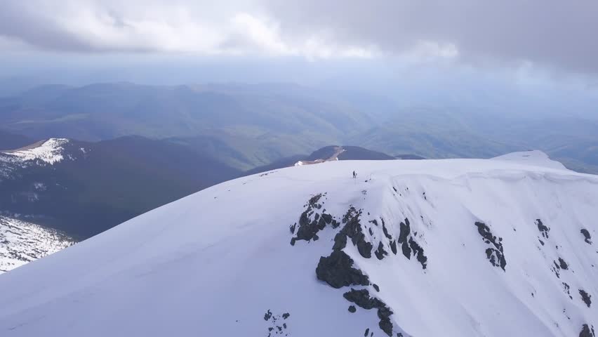 Stunning aerial view of winter mountaintop landscape. Show covered mountains and deep valley beyond seen from drone orbiting man on Carpathian mountain peak.