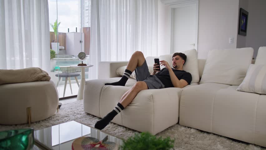 Sleepy young man brownsing on his phone until he falls asleep. Man lying on the couch at home on a lazy morning Royalty-Free Stock Footage #1108252593