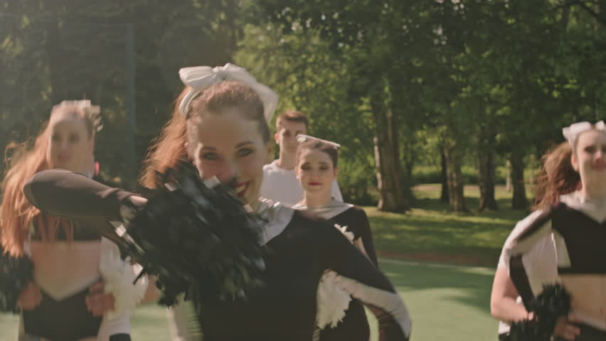 Slow mo shot of cheerleading girls smiling on camera and dancing with pompoms, their teammates performing partner stunts, then boy doing backflip on outdoor football field | Shutterstock HD Video #1108252815
