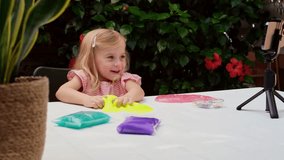 Blonde caucasian girl with playing with slime and watching video instruction on phone. Online education, classes at home, on distance. Child sensory development, modern technologies in childhood.