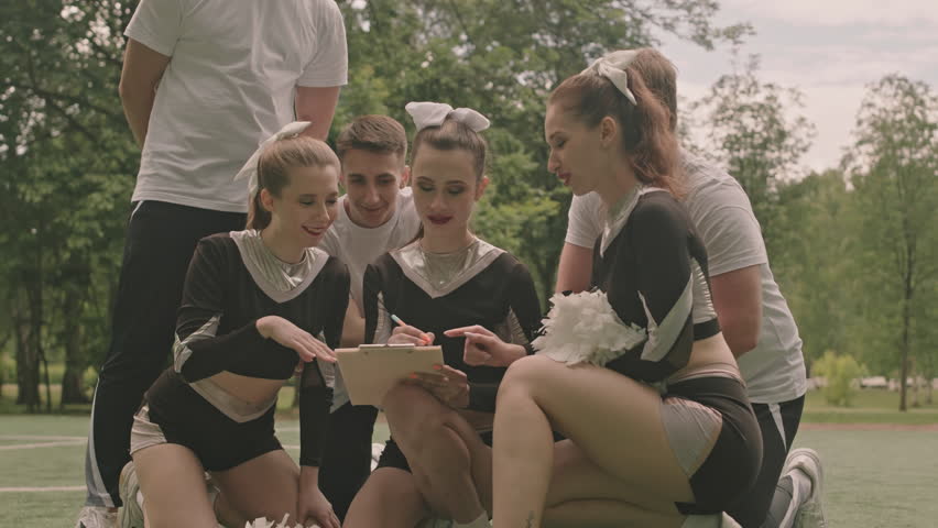 Cheerleading squad having discussion and making notes on paper while preparing for performance on outdoor field | Shutterstock HD Video #1108253225