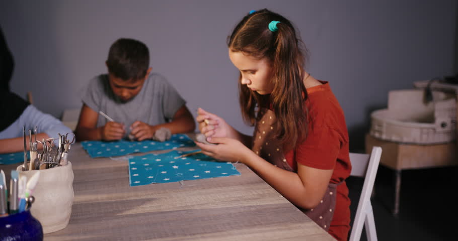 Group of children sculpts clay toys. Hindu and Caucasian pupils engages in sculpting at class in art studio. Kids work with tools forming figures