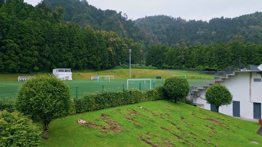 Football field at green forest nature. Aerial view vivid grass soccer stadium slow motion. Sport playground at gloomy daylight. Empty game soccer lawn hidden in national woodland. Sportive location
