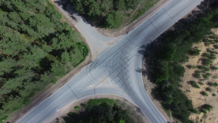 Road junction surrounded by trees, shrubs taken by drone. Cars drive along highway intersection in forest, countryside. Summer, sunny day. Aerial view of traffic on roadway crossing. 4K UHD 2160p Royalty-Free Stock Footage #1108260769
