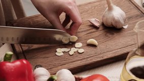 Close-up of a woman cutting fresh garlic with a knife in the kitchen. Preparing vegetable salad. Housewife chopping garlic with knife on wooden cutting board