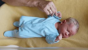 Tiny newborn in blue romper lying on the yellow blanket. Male hand touching the kid's fist. Close up. - Powered by Shutterstock - Get 15% off with code: PIKWIZARD15