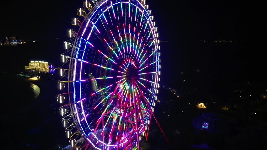 Top view aerial of ferris wheel in amusement park at night. Ferris wheel lights in the evening amusement park, ferris wheel lights. Ride on carousel represents entertainment and fun. 4K.