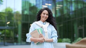 Portrait of smiling female student holding books, textbooks, looking at camera while standing in the campus space near the university building. Happy curly brunette girl posing on the street Head shot - Powered by Shutterstock - Get 15% off with code: PIKWIZARD15