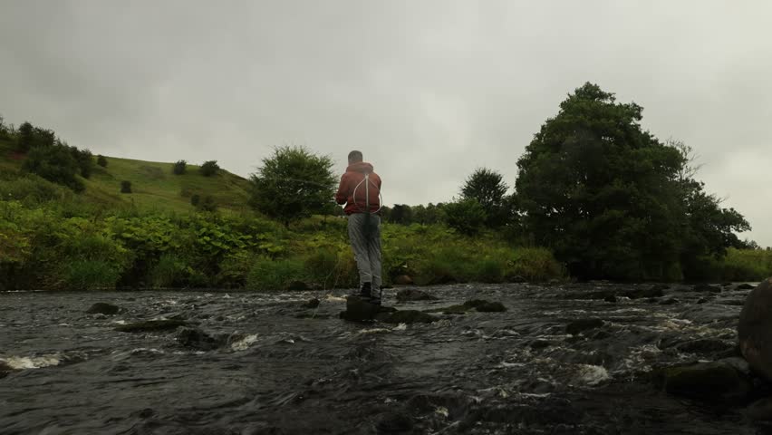 Low-angle shot of a fisherman standing on a rock and casting into a small stream
