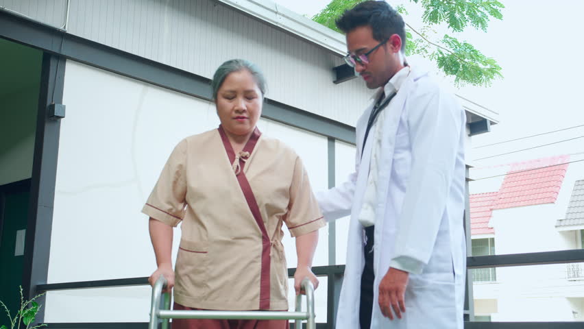 Young doctor assistance elderly patient while guidance therapy with walker in garden at hospital, caregiver or physician support senior and practicing walking with walker, medical and rehabilitation. | Shutterstock HD Video #1108274393