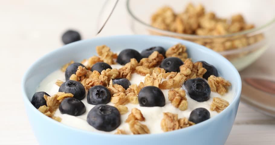 Granola is mixed with a spoon with yogurt and blueberries. Cooking breakfast with muesli and berries. Healthly food.