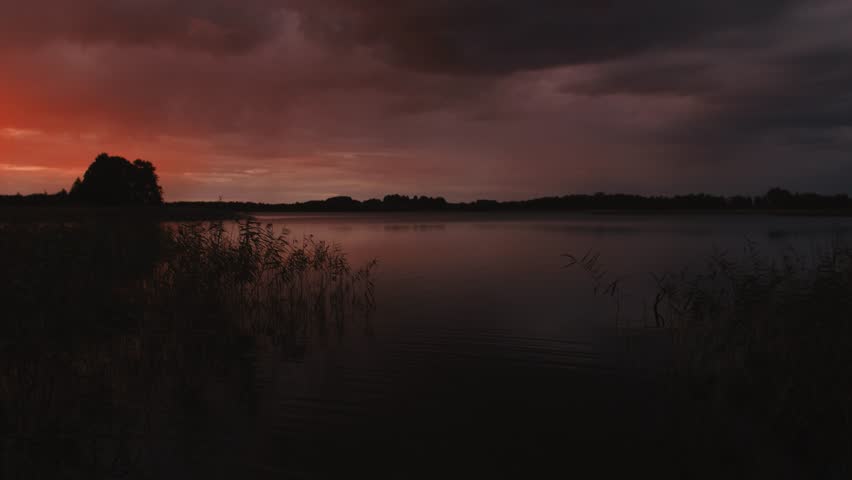 Beautiful sunset over lake in the evening, peaceful calm place. Beautiful Purple Pink Sunset Dramatic Clouds Over Silhouette Of Coastline At Lake or river