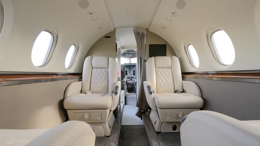 Exquisite interior of private vip aircraft with four white cozy leather seats. Bright cabin with round portholes, ceiling lights and black monitor on wall Royalty-Free Stock Footage #1108279939