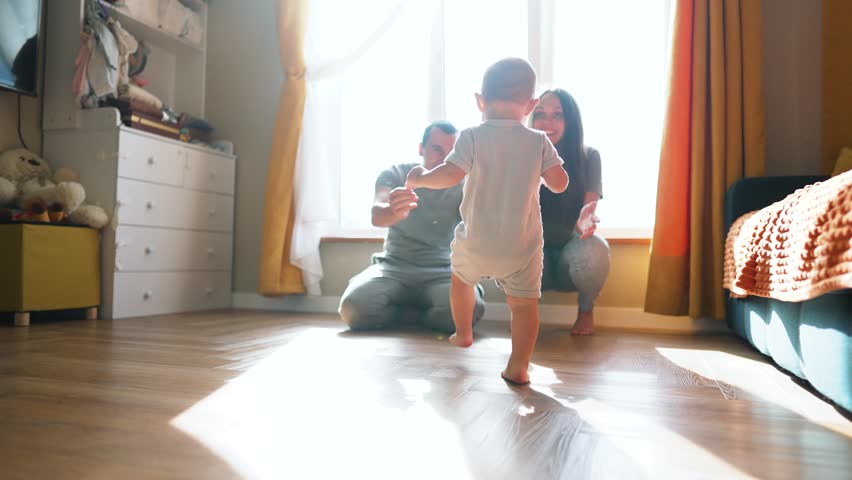Baby first steps.Child kid runs across floor to family.kid learn to walk and run with help of his parents.Happy family at home first steps of toddler.father encourages baby teaches to take first steps