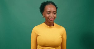 Young Black woman raises hands, yells excitedly, green background studio