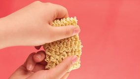 Vertical video of hands crashing instant noodles on red background with copy space