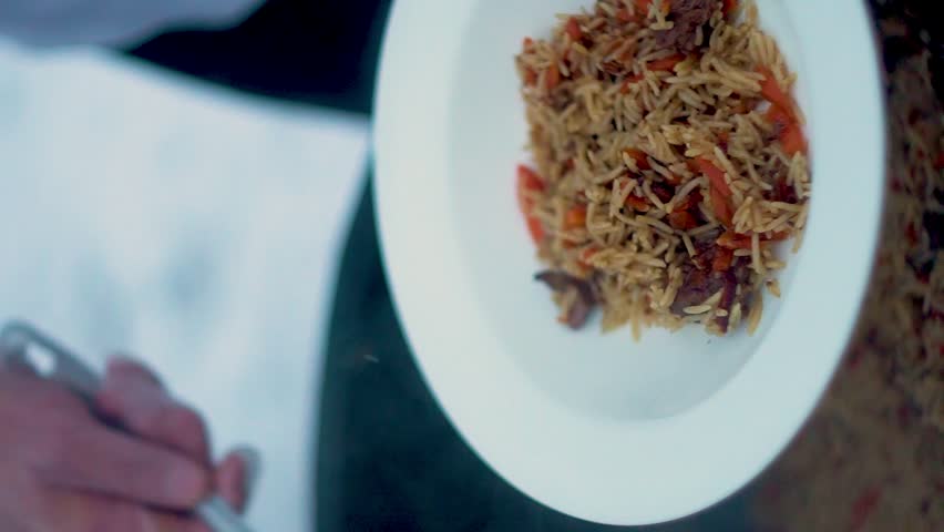 Cooking traditional pilaf in a cauldron in nature, outdoors. Eastern, oriental national rice dish, Uzbek cuisine. Uzbek pilaf of beef, lamb, chicken in a large cauldron with vegetables. Vertical video