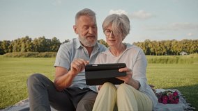 Cute family couple of senior age sitting on street carpet with digital tablet in hands and doing internet shopping. Casually dressed man and woman advising together and choosing items for house. - Powered by Shutterstock - Get 15% off with code: PIKWIZARD15