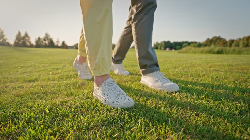 Close up of elderly man and woman in white sneakers walking together on green grass. Happy people in love keeping body in good shape while exploring new tourist destinations.
