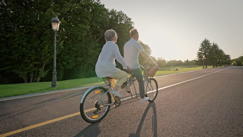 Back view of elder couple traveling on riding path with double bicycle. Senior man and woman engaging in healthy lifestyle while moving near golf course. Concept of retirement and transport. Royalty-Free Stock Footage #1108288129