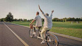 Back view of elder couple traveling on riding path with double bicycle. Senior man and woman engaging in healthy lifestyle while moving near golf course. Concept of retirement and transport. - Powered by Shutterstock - Get 15% off with code: PIKWIZARD15