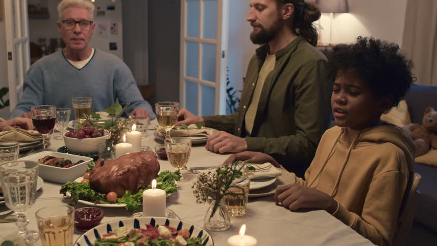 Intercultural members of family holding each others hands and praying before festive dinner in cozy living room | Shutterstock HD Video #1108290431