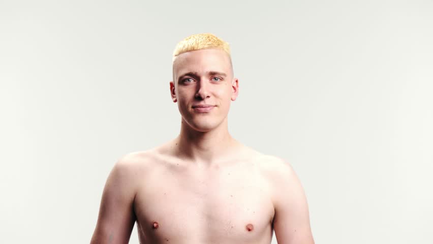 Young shirtless man being covered with thick blue paint against white studio background. Paint splash. Abstract art on human body. Concept of creativity, inspiration, fun, emotions