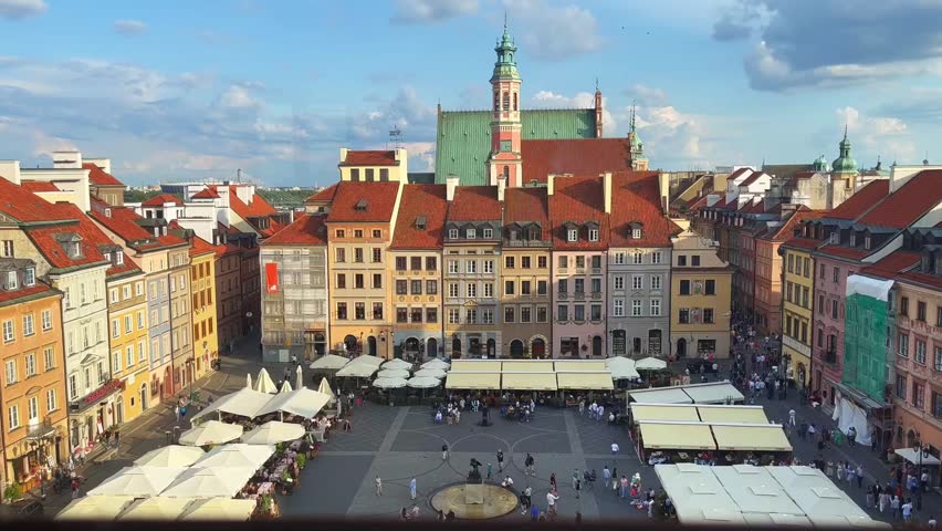 A view of the Old Town market square in Warsaw. People stroll along the paving stones among summer cafes, white umbrellas and fantans in the atmosphere of colorful houses of the old town