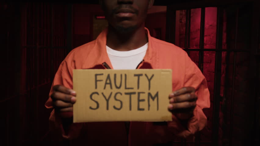 African American man in jail uniform holds cardboard with phrase Faulty System Royalty-Free Stock Footage #1108297255