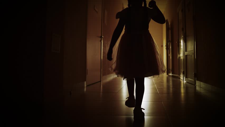 Lonely silhouette of child running down dark corridor towards door and light. Girl child in dark empty corridor. Little girl looks out of window, rear view. Primary school looking to future of child Royalty-Free Stock Footage #1108301165