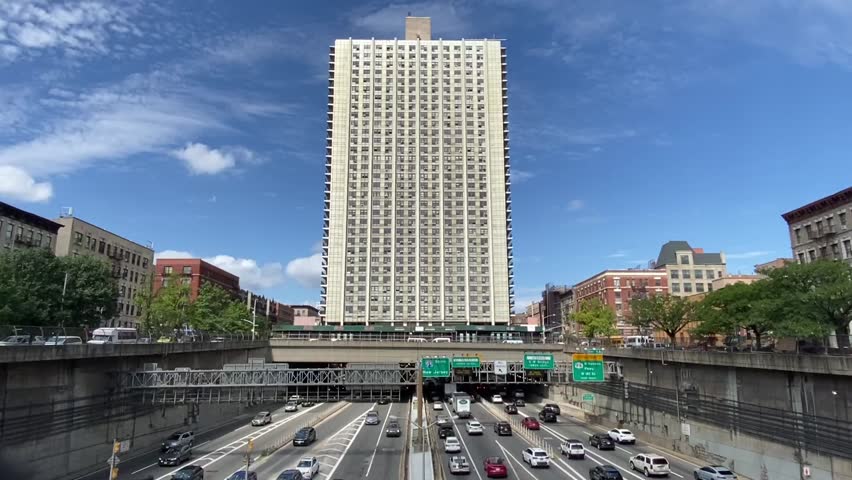 Establishing shot from above of traffic on the Trans-Manhattan Expressway (I-95) passing under the Bridge Apartments on a sunny day in Washington Heights, Upper Manhattan, New York City