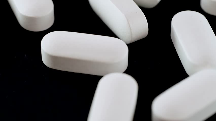 White oblong medical pills close up tracking shot on isolated dark background. Pharmaceutical Industry. Medicine concept. Camera movement drugs and tablets. 