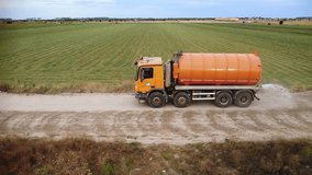 Aerial drone tracking footage of dust suppression truck spraying water on a dusty rural haul road. Construction machinery off road. Dust management. Pollution control. 