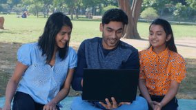 A happy Indian family watching a comedy movie in an open area - movie time, entertainment. A young family enjoying a funny video playing on a laptop in the park - laughing out loud, young adult, la...