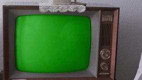 elderly man turns on and watches old retro analog TV with blank green screen for designer, entertainment, leisure essential of life older individuals, Technology 1960-1970, mockup, template for video