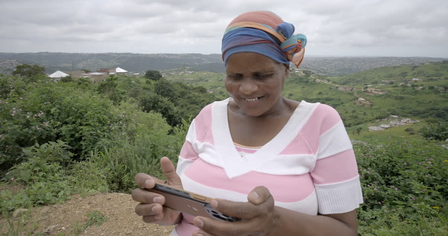 Close up of a black African woman laughing while watching a video on her mobile phone in a rural Zululand setting. Royalty-Free Stock Footage #1108320029