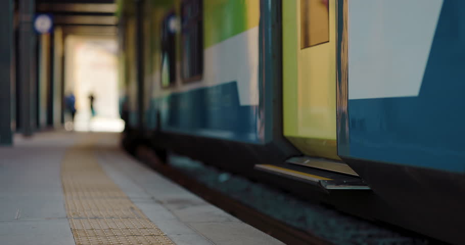 Close up of the carriage door of a modern train. Legs, female or male feet of passengers getting on and off the carriages. with trolley or without luggage. Background: rural village with green nature
