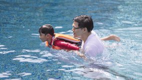 Asian family swimming in the pool on a happy vacation. A father teaches swimming to his child wearing a life jacket. Summer vacation activities - Powered by Shutterstock - Get 15% off with code: PIKWIZARD15