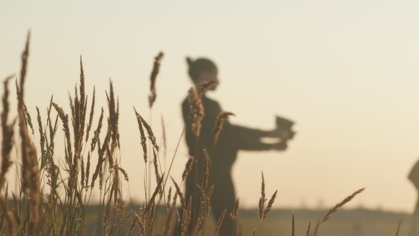 Slowmo of couple of professional artists rehearsing for extreme fire show performance in field at sunset with wheat fluttering in wind in focused background | Shutterstock HD Video #1108332335