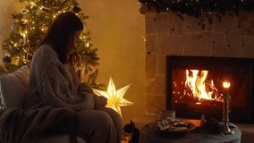 Woman with pets relaxing at cozy at fireplace in eve. Woman in cozy sweater hugging cute cat and playing with adorable dog at burning fireplace in christmas festive room. Footage