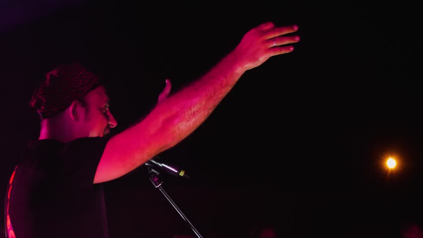The lead singer of a rock band singing into a microphone and spreading his arms out to the sides. Close-up, side view. The performance of the band on the night stage of the club Royalty-Free Stock Footage #1108334965