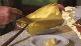 close-up of a female hand opening the ready-made tamale. Hand removing the straw from the finished pamonha. Brazilian traditional food. dish of traditional food of festa junina. Theme video collection