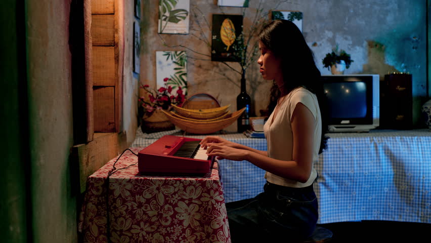 Asian girl playing keyboard at home, static side view
