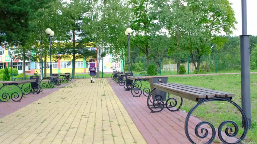 Cheerful funny girl with toothless smile in school uniform with white bows running in school yard. Back to school, September 1. Happy pupil with backpack. Primary education, elementary class. motion