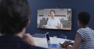 Diverse business people on video call with caucasian male colleague on tv screen. Online connections, business and networking concept.