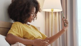 Smiling Black African American Pregnant woman holding showing ultrasound scan photos. Expecting mother having video call with family on smartphone at bed. - Powered by Shutterstock - Get 15% off with code: PIKWIZARD15