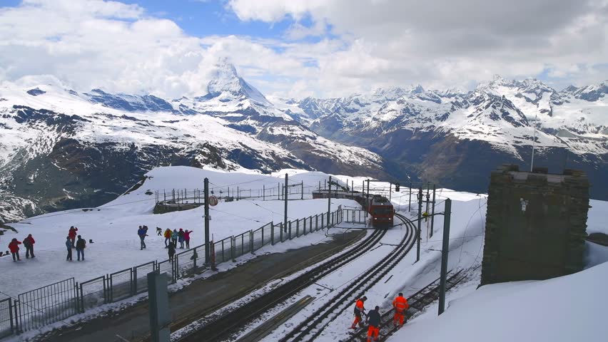 Gornergrat, Zermatt May 22,2023:Red train on snowy railway at summit station with tourists and Matterhorn summit in Switzerland