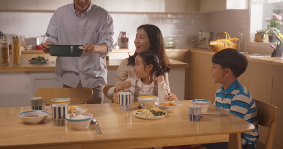 Happy Korean Family of Four Enjoying a Delicious Meal Together in Their Kitchen at Home. They are Sharing a Traditional Meal Made with Love and Care. Children Excited for Food
