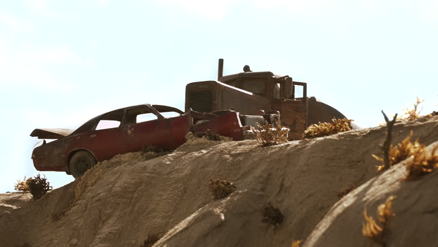 USA, California, up angle of rock cliff with blue sky above. 70's red car with fire in its trunk chased by a 50's rusty threatening tanker truck tumbles over a cliff. Car spins. 1:18 scale models. Royalty-Free Stock Footage #1108358325