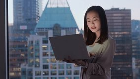 Young confident busy Asian business woman executive holding laptop in dark office. Professional businesswoman manager using computer standing at window with big city evening view. - Powered by Shutterstock - Get 15% off with code: PIKWIZARD15
